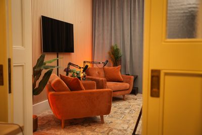Sofaopstelling met twee oranje stoelen en microfoons in Podcast Studio 010