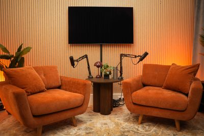Twee oranje sofastoelen met twee microfoons op een centrale tafel, tv aan de wand
