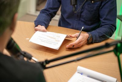 Gast met aantekeningen aan tafel tijdens podcast opname